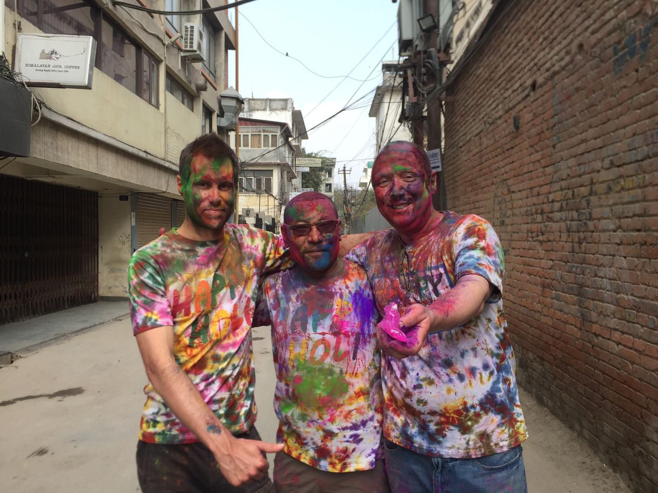 Three guests covered head to toe in bright Holi colours, laughing together
