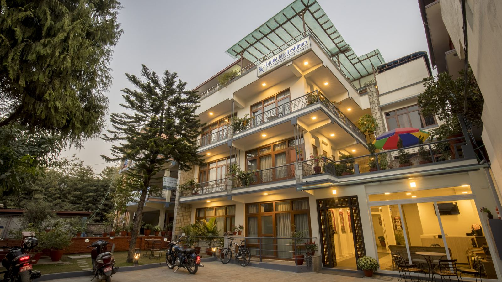 Karma Tara Residency at dusk — lit balconies, glass-roofed lounge and courtyard garden