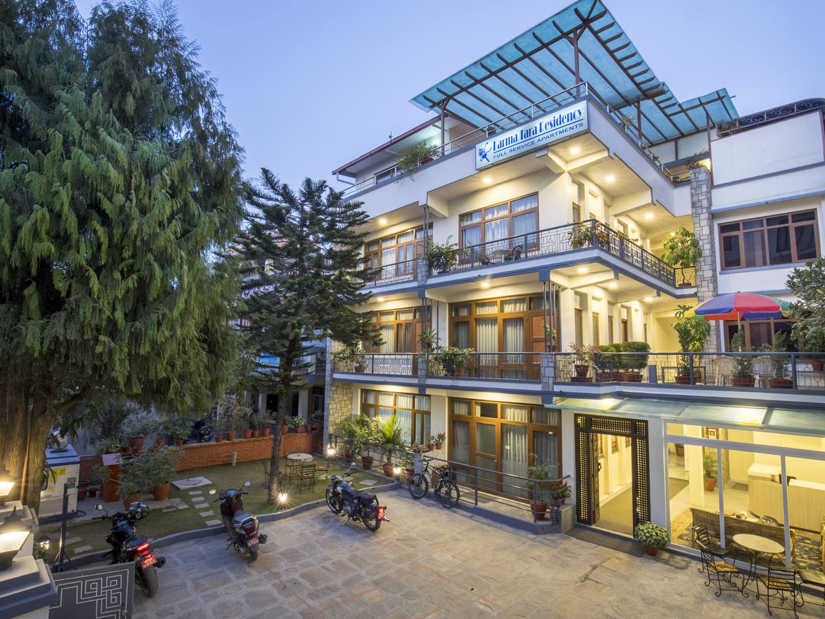 The Karma Tara residence at dusk — glass-roofed terrace, lit balconies, garden and pine tree